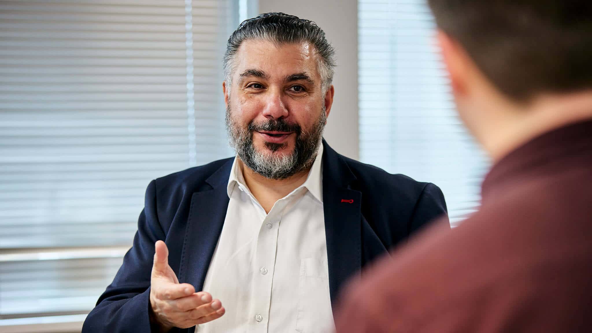 George Georgiou in blue jacket gesturing with right hand