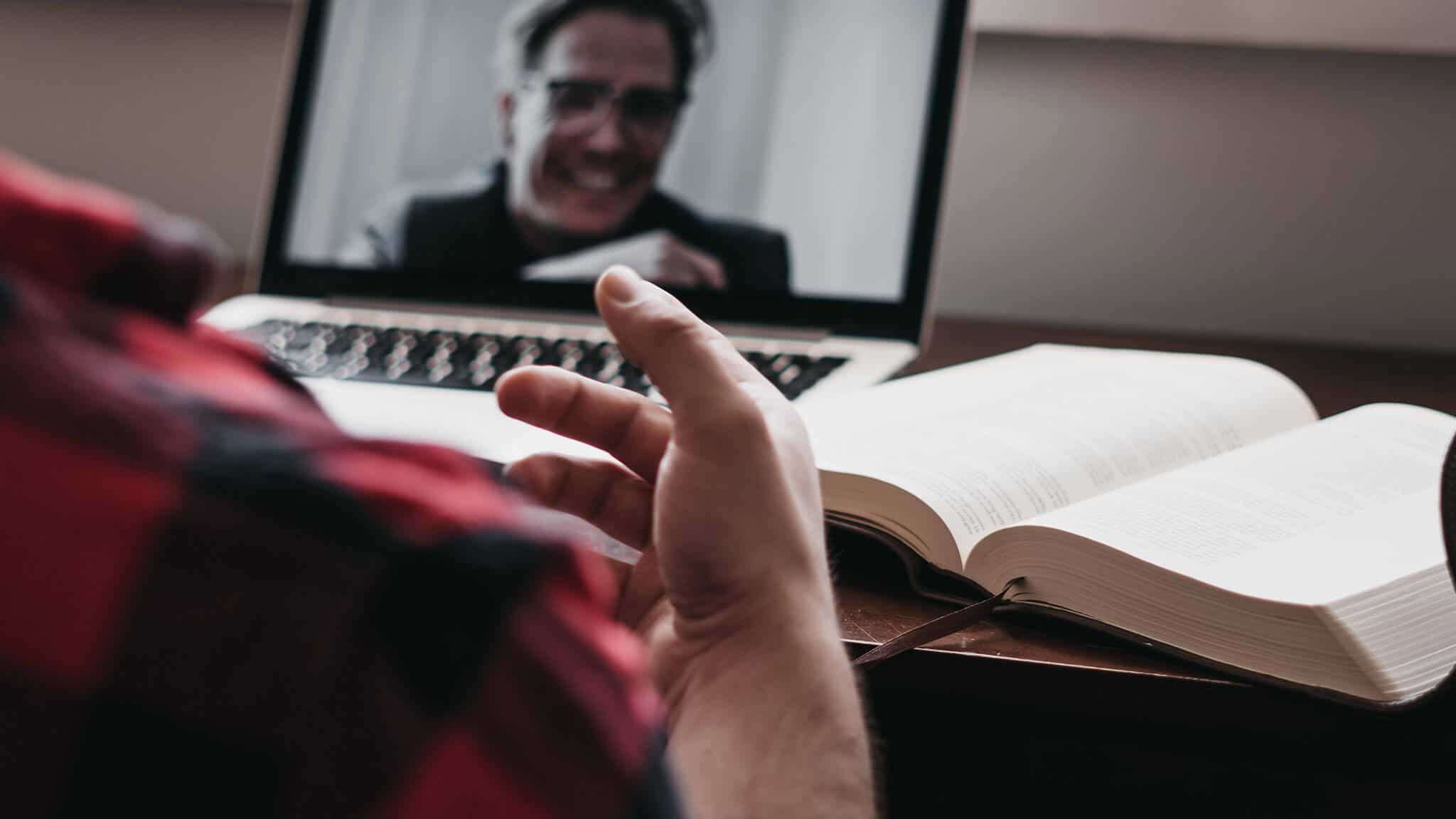 Over the shoulder shot of man's hand, open book, and laptop