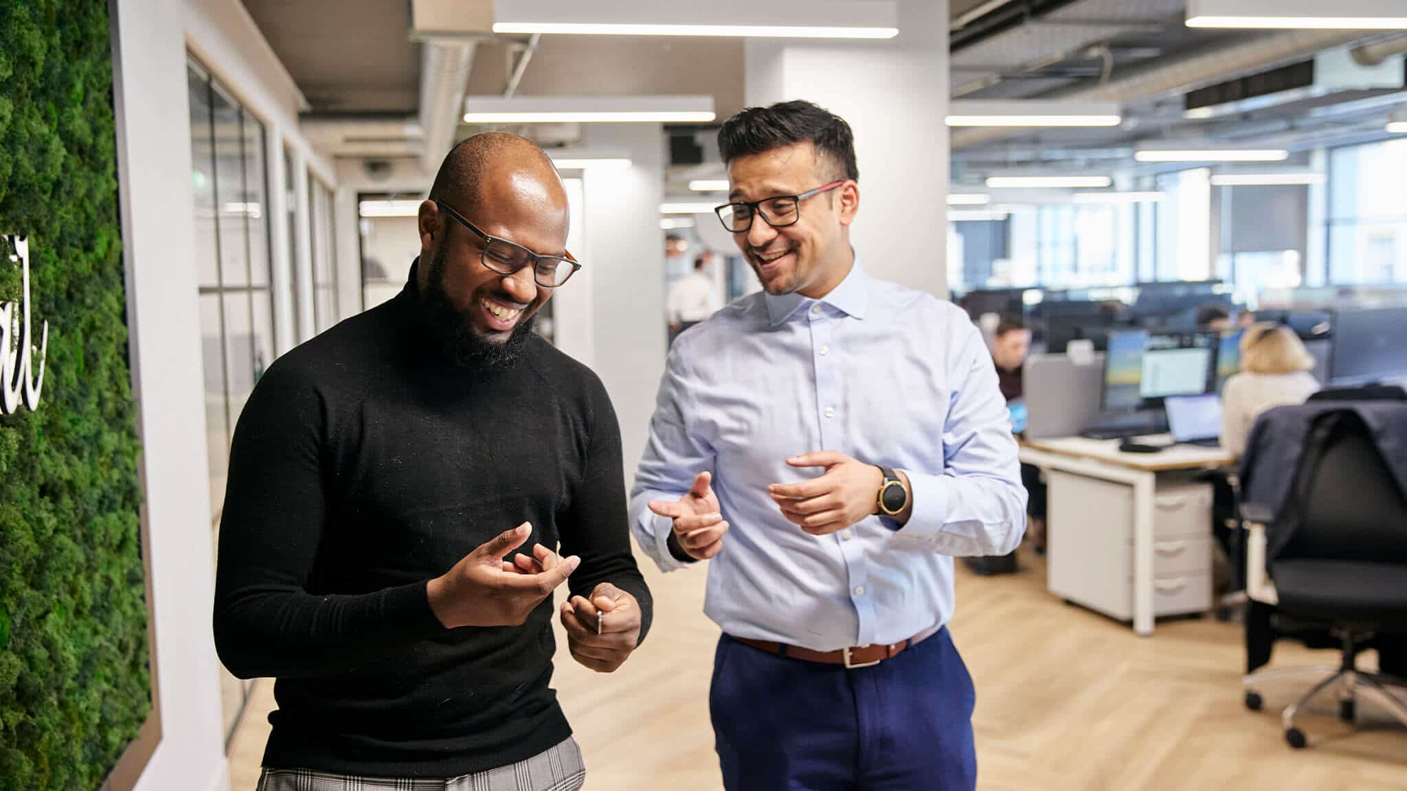 Two men walking towards the camera laughing in office